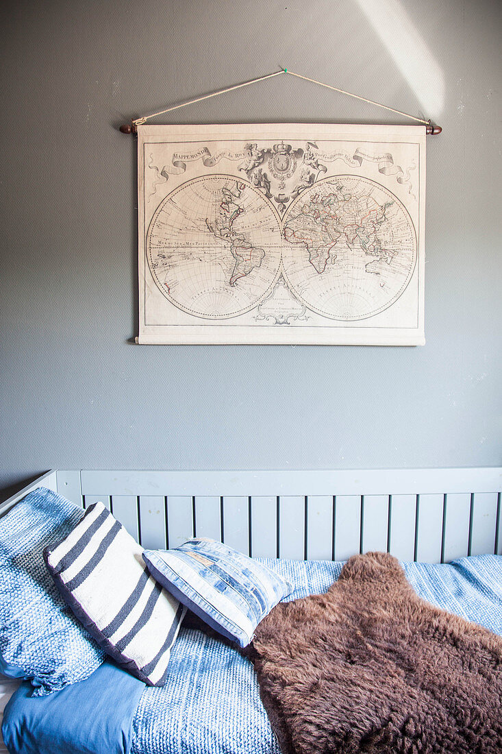 Bett mit Bettwäsche im Blau und Tierfell, darüber Vintage Weltkarte