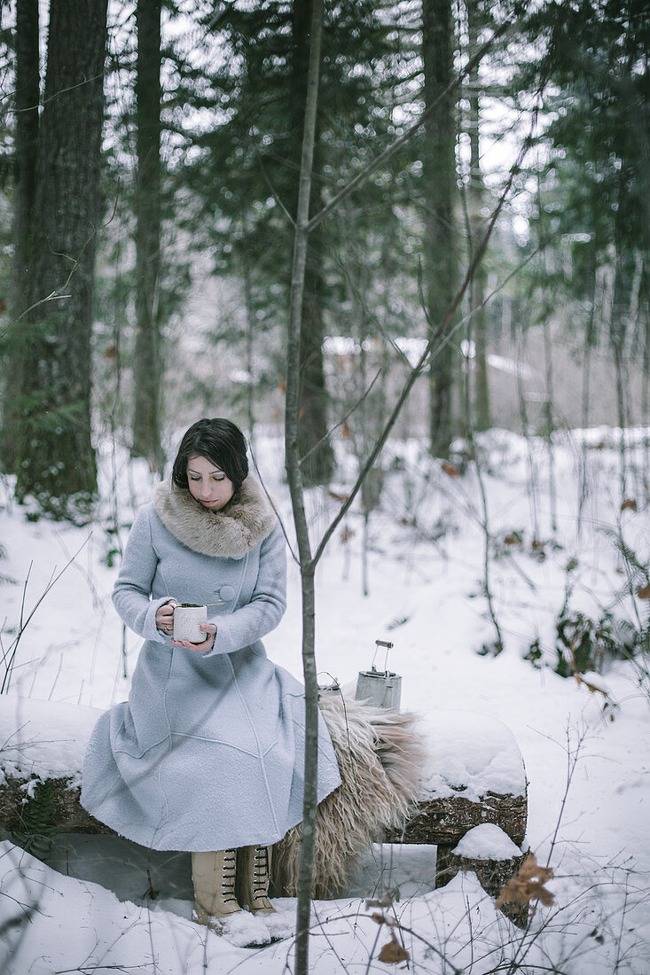 Frau trinkt Tee im verschneiten Wald