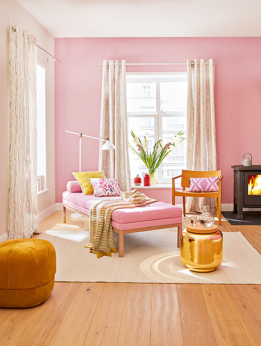 Daybed, Stuhl, Holzofen, goldfarbener Beistelltisch und Pouf im Wohnzimmer in Rosatönen