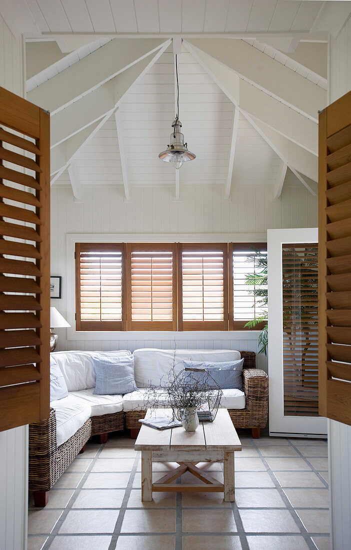 Korbsofa im gefliesten Wohnzimmer im Strandhaus-Look mit hoher Decke