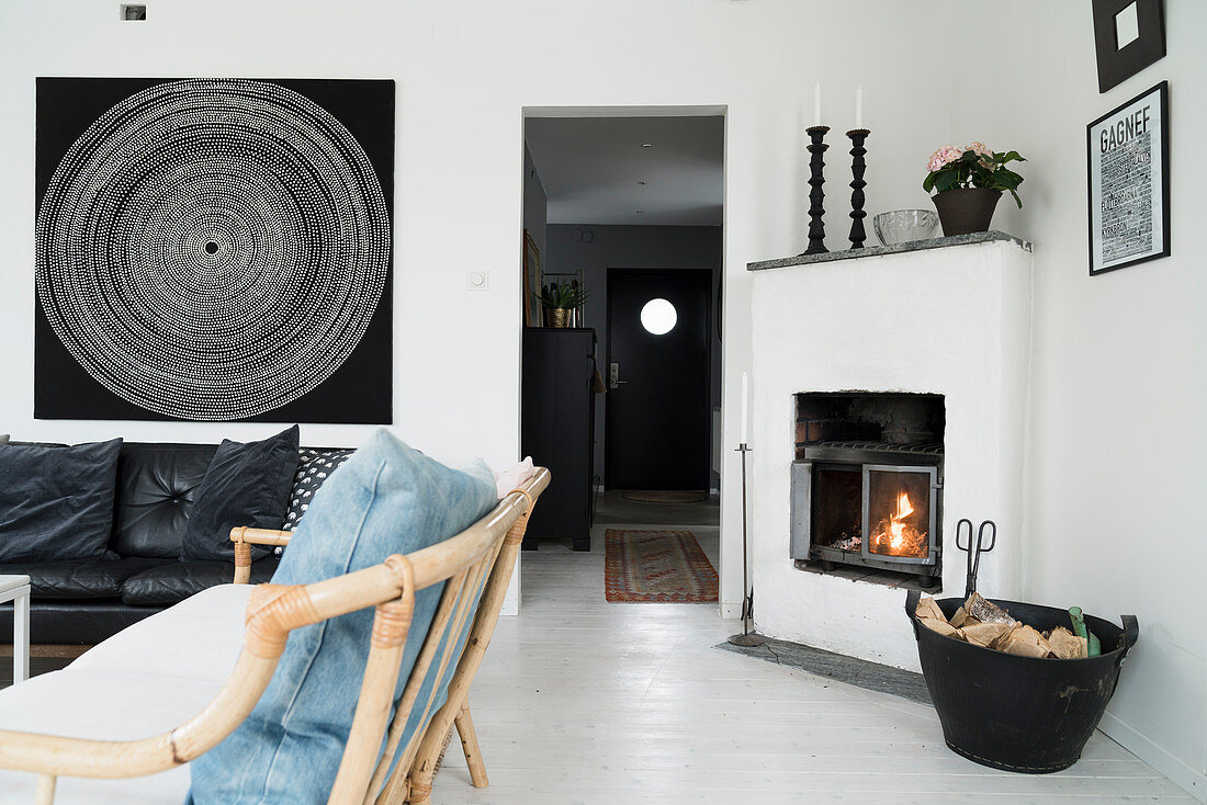 Fireplace in white living room with black leather couch and rattan sofa