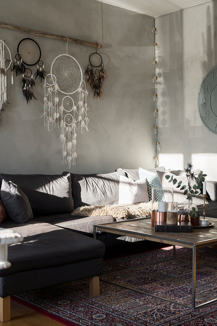 Coffee table, sofa, dreamcatchers on wall, armchair and screen in living room with pale grey walls