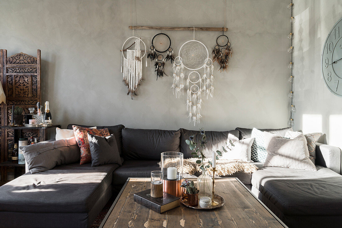 Couchtisch, Sofa, darüber Traumfänger, Sessel und Paravent im Wohnzimmer mit hellgrauer Wand