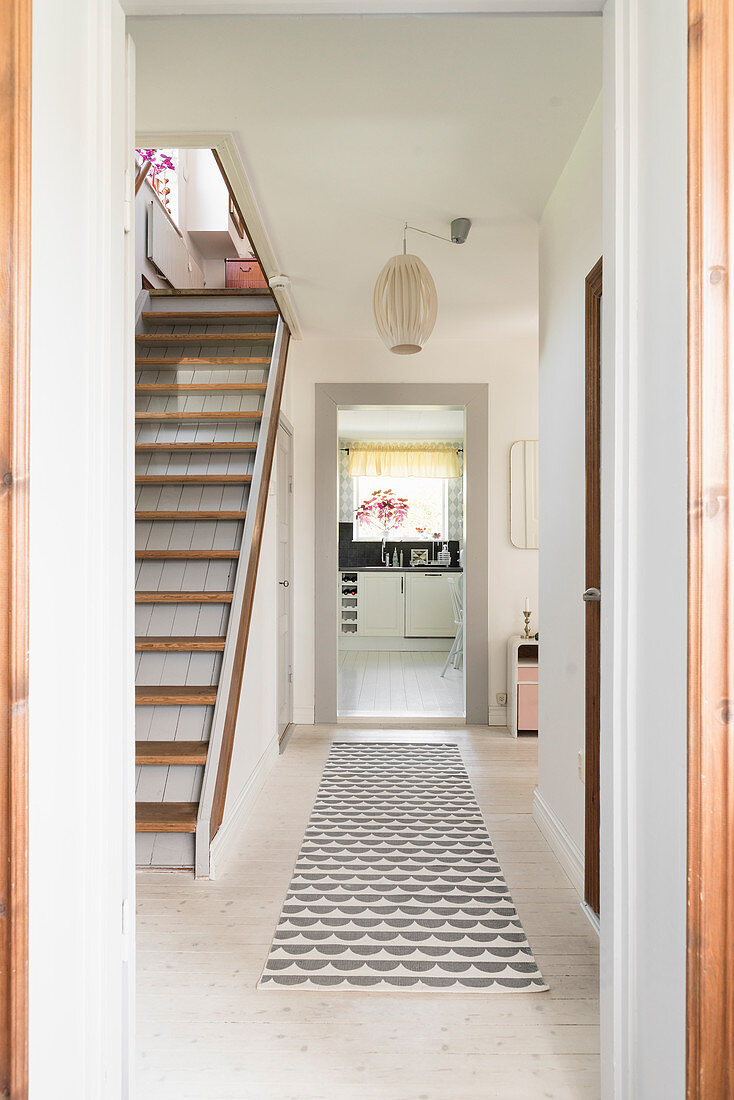 Pale wooden floor and staircase in hallway with view into kitchen at far end