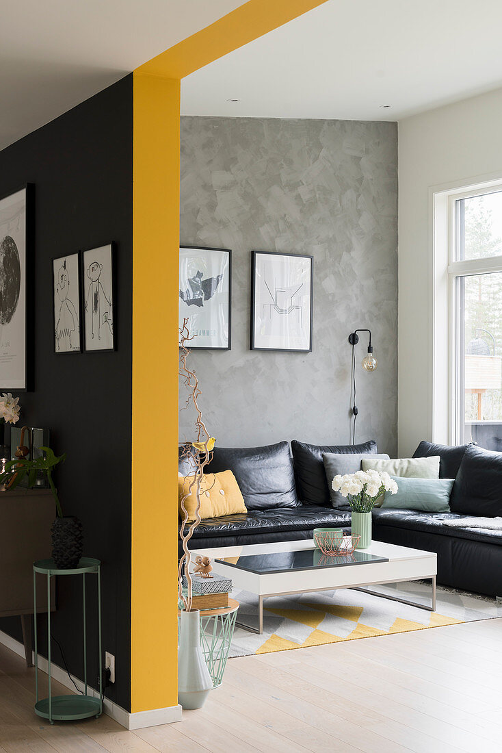 Blick auf schwarze Ledercouch an grauer Wand in offenem Wohnraum