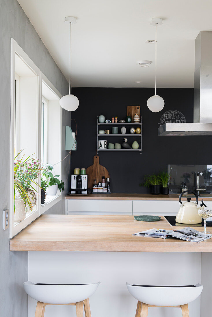Blick über Kochtheke mit heller Holzplatte auf Küchenzeile vor anthrazitfarbener Wand