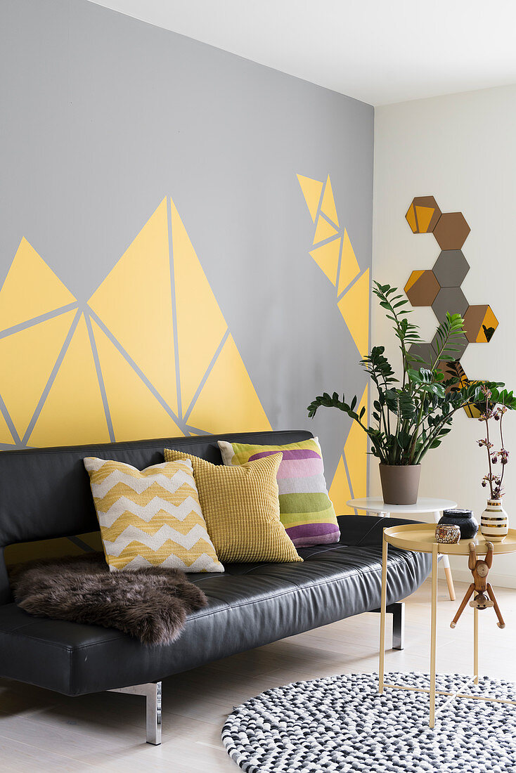 Schwarze Ledercoucht und Beistelltische im Wohnzimmer mit grau-gelber Wand