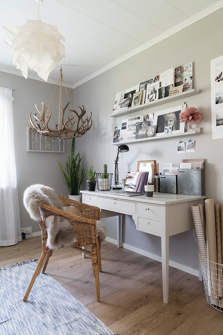 White desk and wicker chair below shelves on grey wall