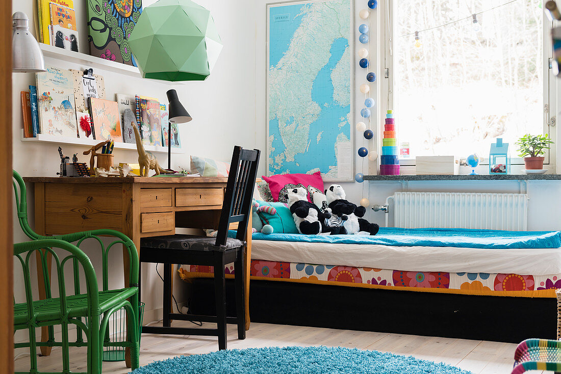 Bett mit Stofftieren, Holzschreibtisch und Stühle im Kinderzimmer
