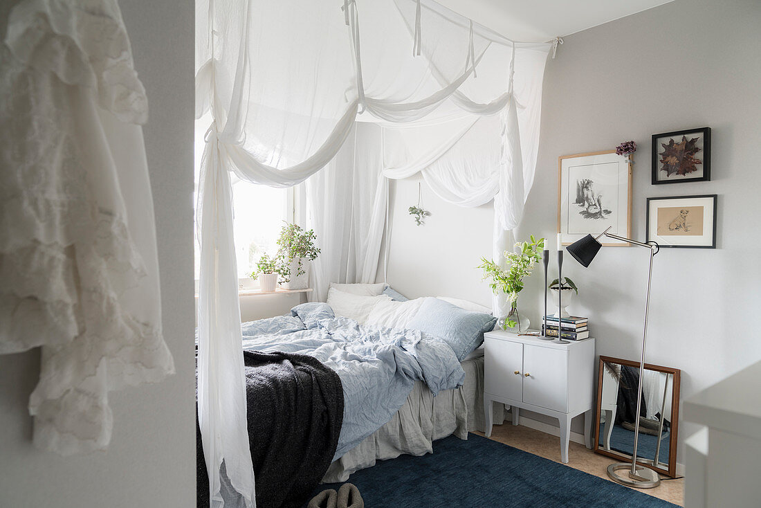 Bett mit weißem Vorhang und Nachtschränkchen in gemütlichem Schlafzimmer