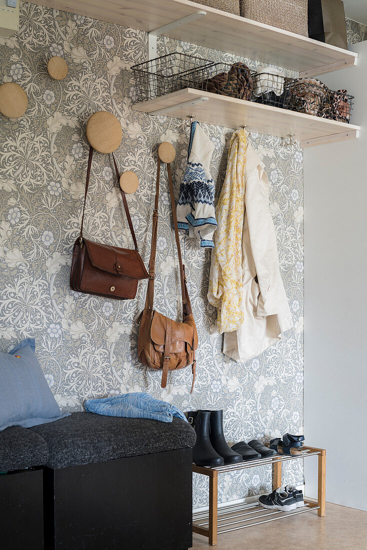 Coat pegs, shelves and cubic pouffes in hallway with patterned wallpaper