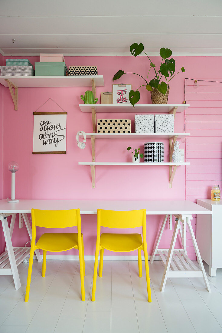 Gelbe Stühle am Schreibtisch vor rosafarbener Wand mit Regalen