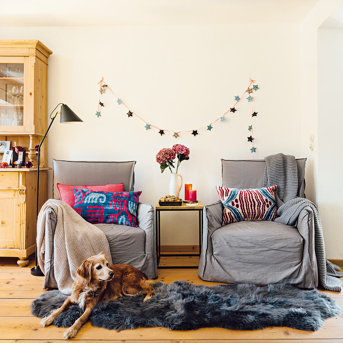 Armchairs and a side table in front of a Christmas garland with a dog lying on a grey animal fur rug