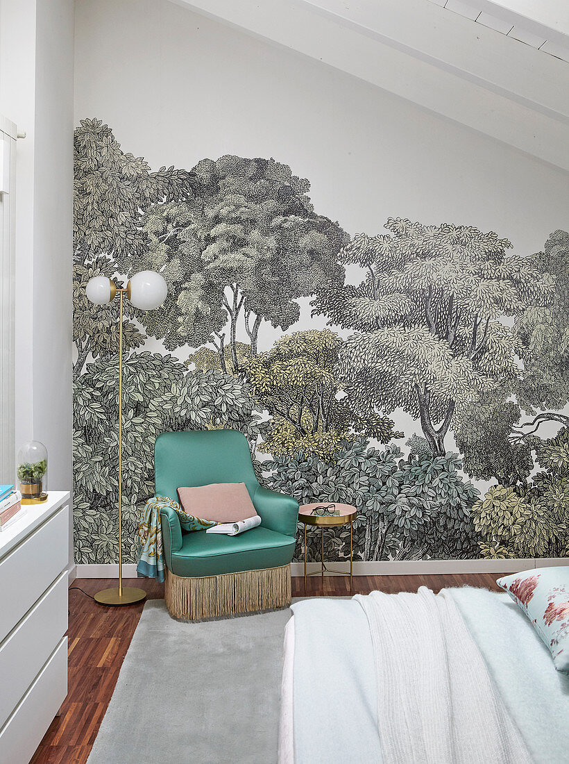 Green armchair against wallpaper with tree motif in bedroom