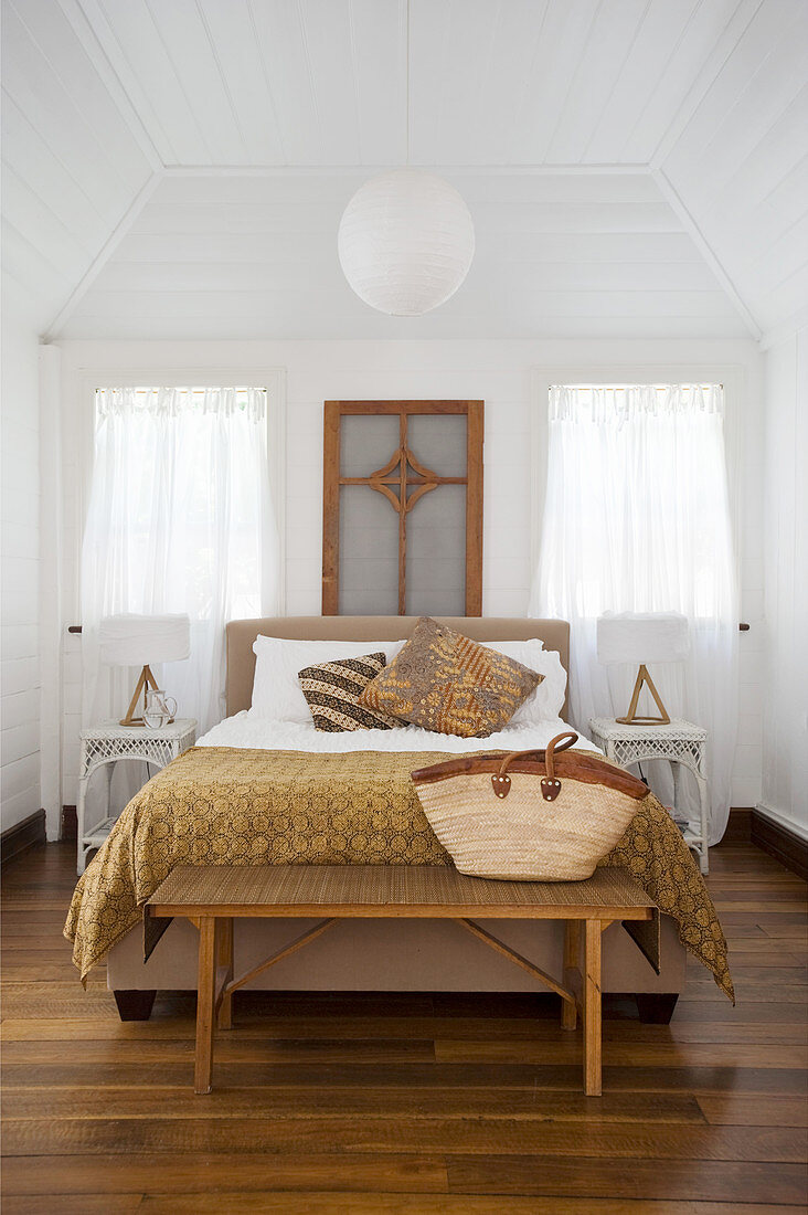 Double bed, bedroom bench, symmetrically arranged bedside cabinets and white-painted wood cladding in bedroom