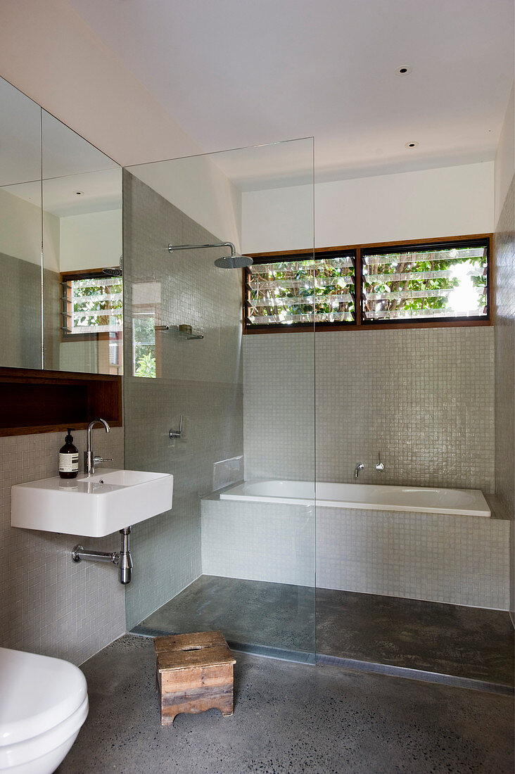 Regendusche und Badewanne hinter Glasabtrennung im Badezimmer mit Mosaikfliesen und Fensterband