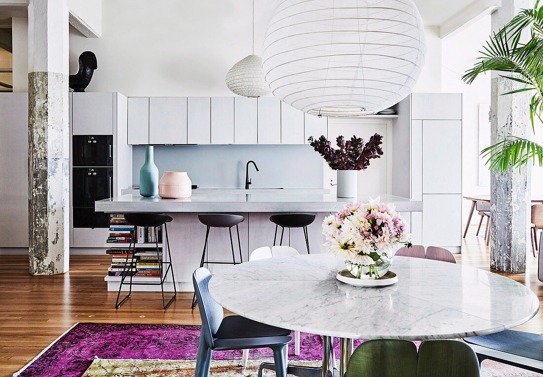 Offener Wohnraum mit moderner weißer Küche, Frühstückstheke und rundem Marmor-Esstisch