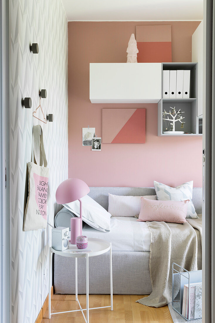 Schlafcouch und Beistelltisch im Zimmer mit Accessoires in Rosa, Hellgrau und Weiß