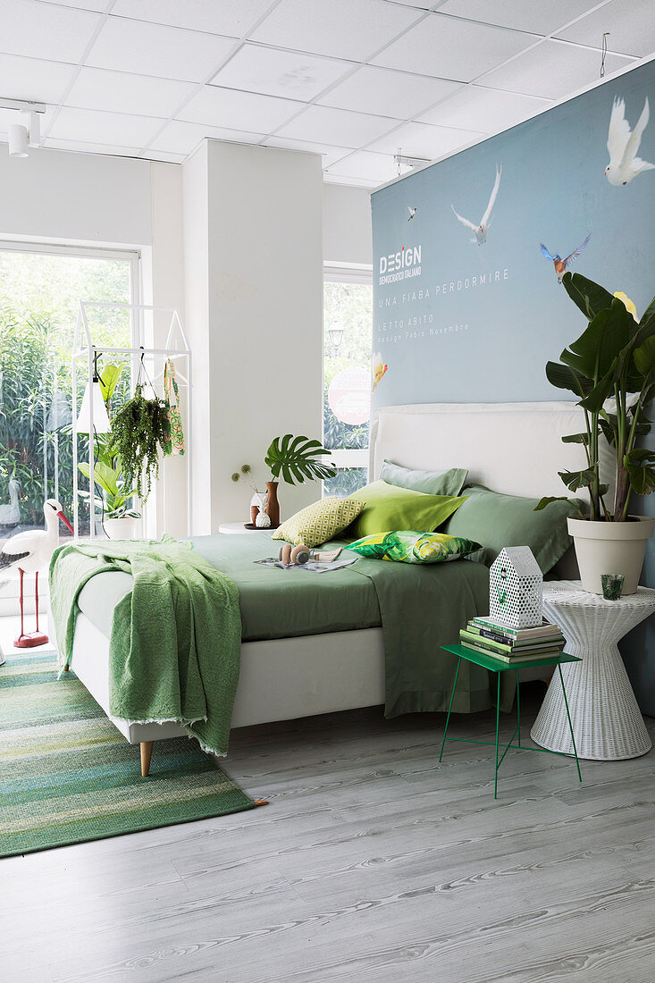 Bettwäsche in Grüntönen auf weißem Doppelbett mit Bettkopfteil in offenem Schlafraum