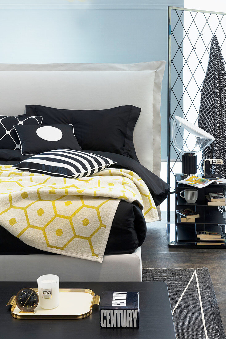 Black-and-white bed linen and yellow blanket on white double bed with headboard
