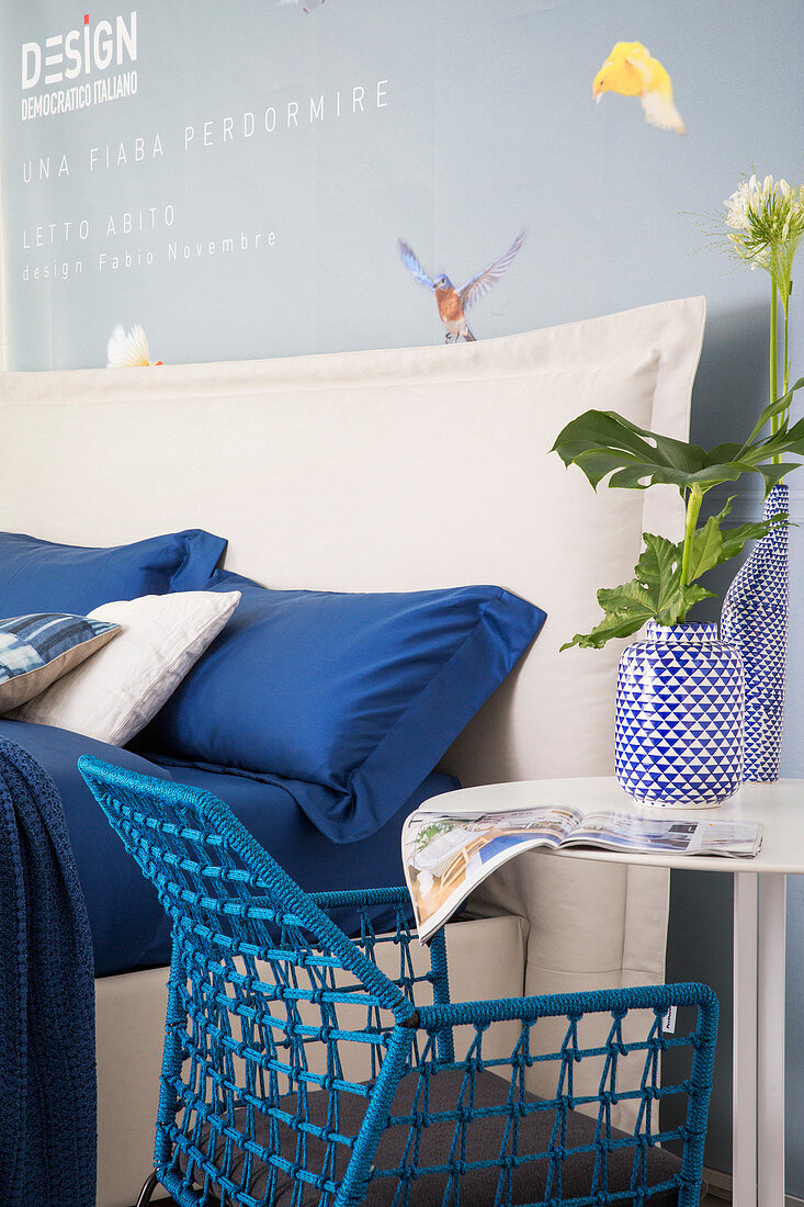 Blaue Bettwäsche auf weißem Doppelbett mit Bettkopfteil, Beistelltisch mit blau-weißen Vasen und blauer Stuhl