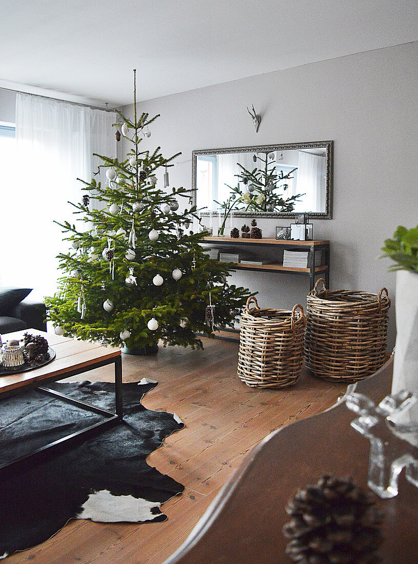 Geschmückter Weihnachtsbaum und Körbe vor Sideboard und Wandspiegel im Wohnzimmer