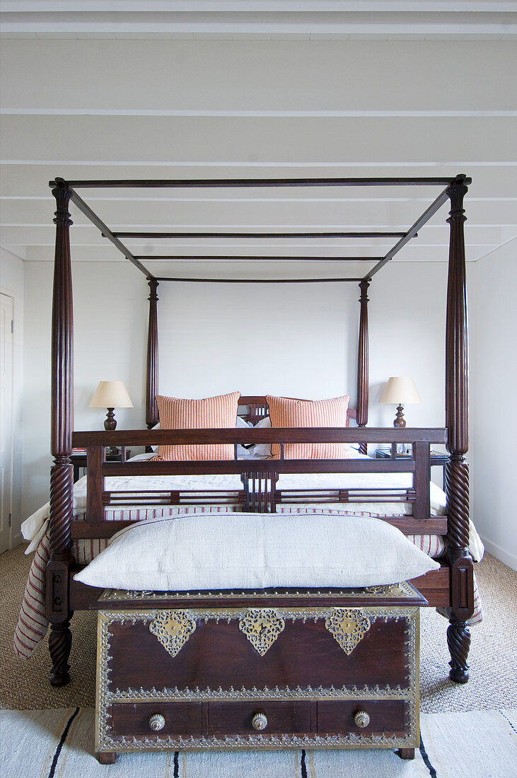 Oriental trunk with large cushion on top at foot of wooden four-poster bed