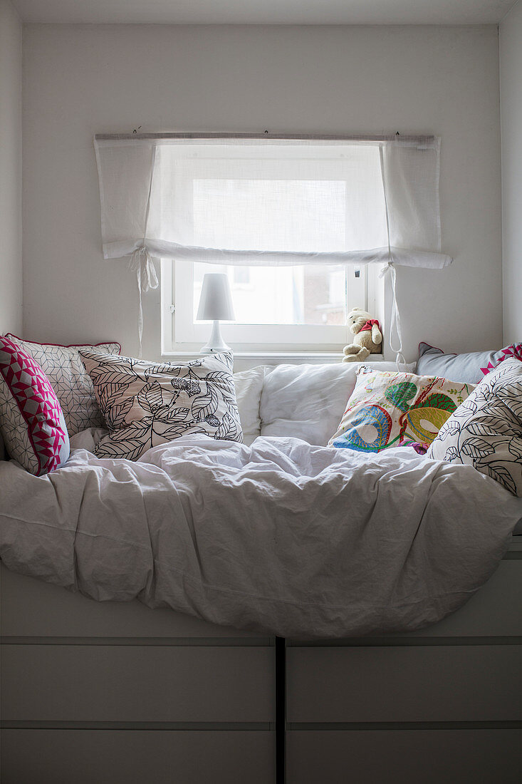 Bett mit vielen Kissen auf zwei Kommoden unterm Fenster