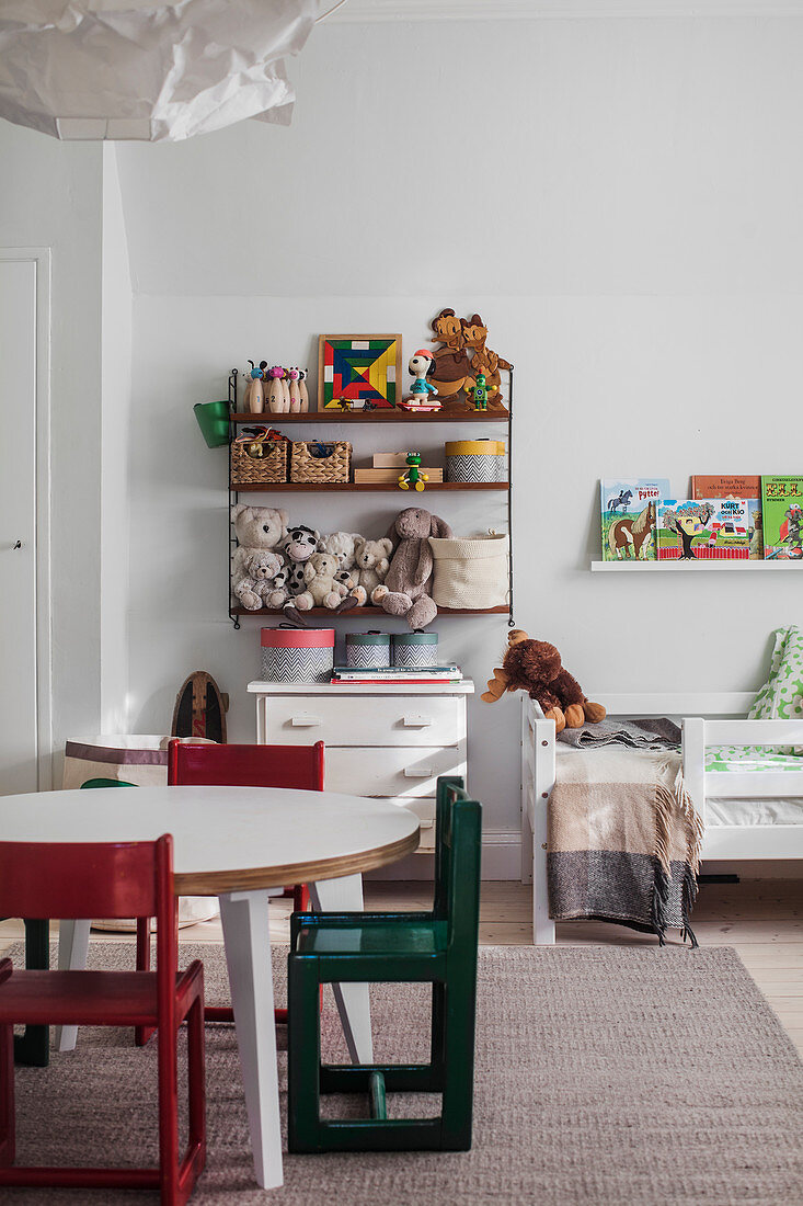 Tisch mit Stühlen, Kommode, darüber Regal mit Spielsachen und Bett im Kinderzimmer