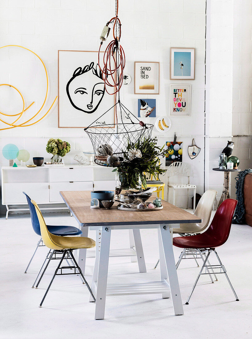 Dining table with colorful chairs, pendant lamp with basket above, modern art on the wall