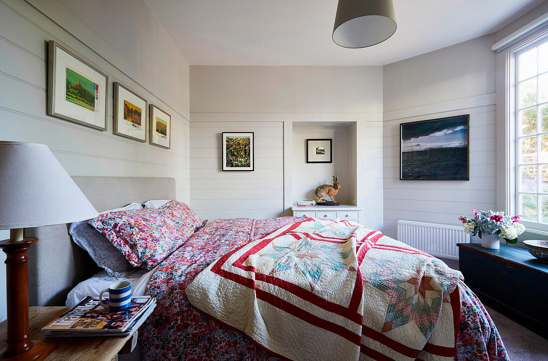 Patchwork-Tagesdecke auf grauem Polsterbett in Schlafzimmer mit weißen Holzwänden