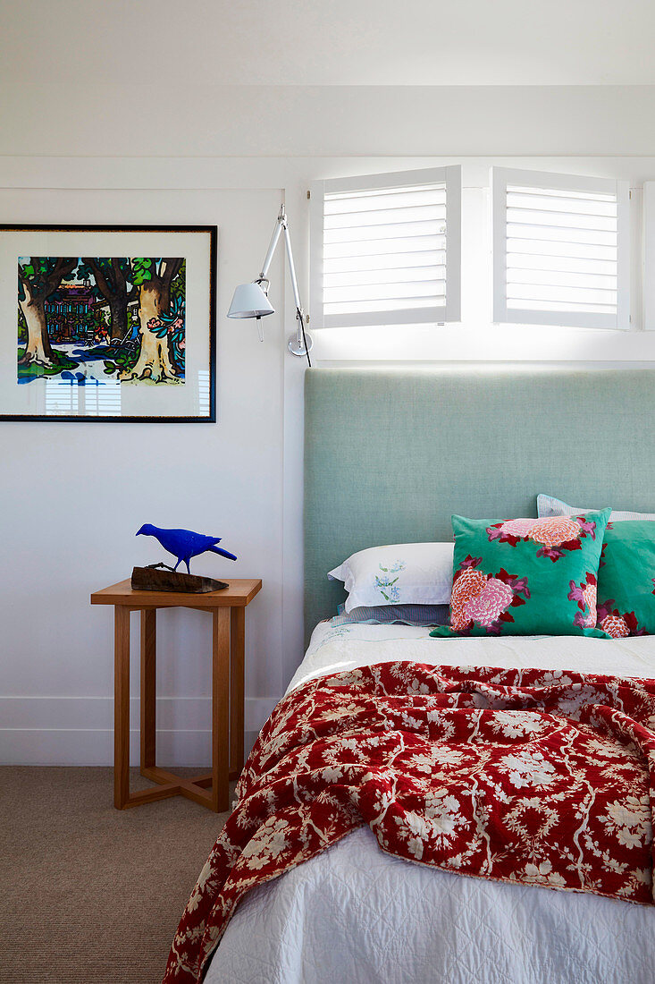 Bett mit hohem mintgrünem Kopfteil unter schmalem geöffneten Lamellenfenster
