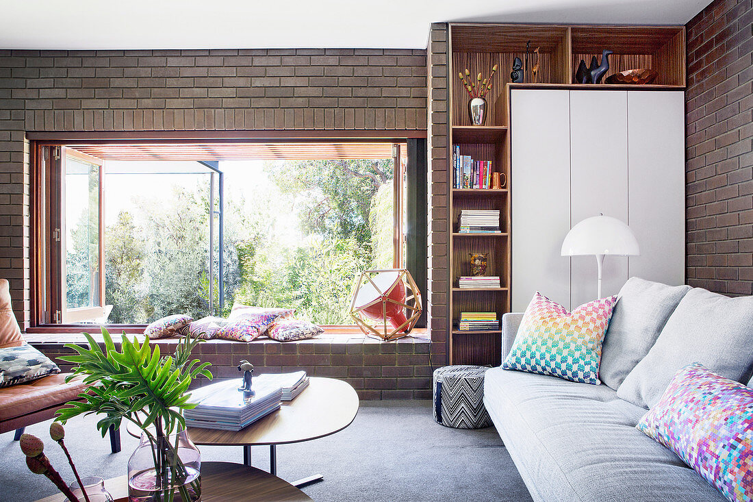 Sofa vor Regal und Schrank und Coffeetable im Wohnzimmer mit geöffnetem Fenster und breiter Fensterbank