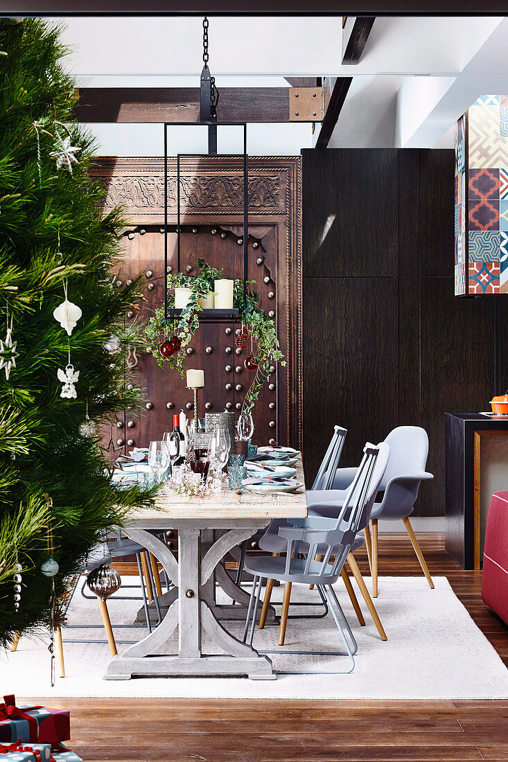 Dining area with gray chairs in front of an antique, Moroccan door as a room divider, decorated Christmas tree in the foreground