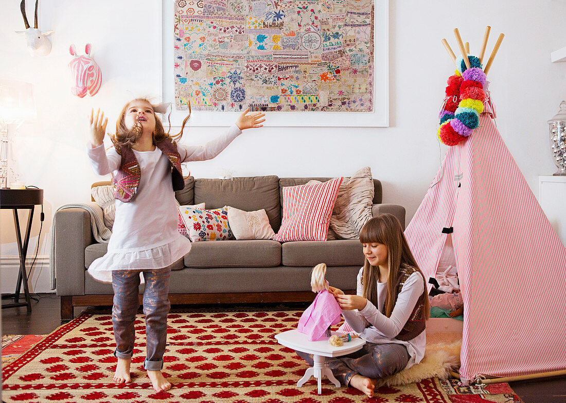 Girls playing on patterned carpet in front of pink teepee in living room