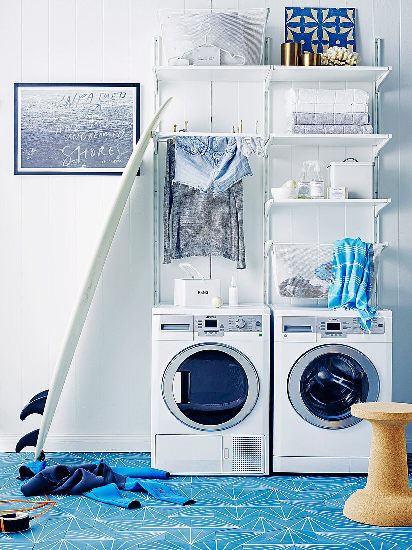 Waschmaschine und Trockner, darüber weiße Regale im Waschraum mit hellblauen Zementfliesen