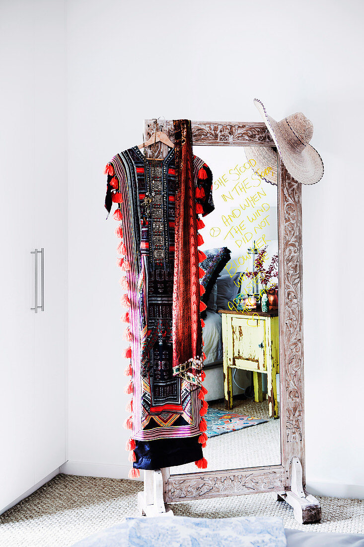 Standing mirror with wooden frame, caftan and hat hung over the mirror