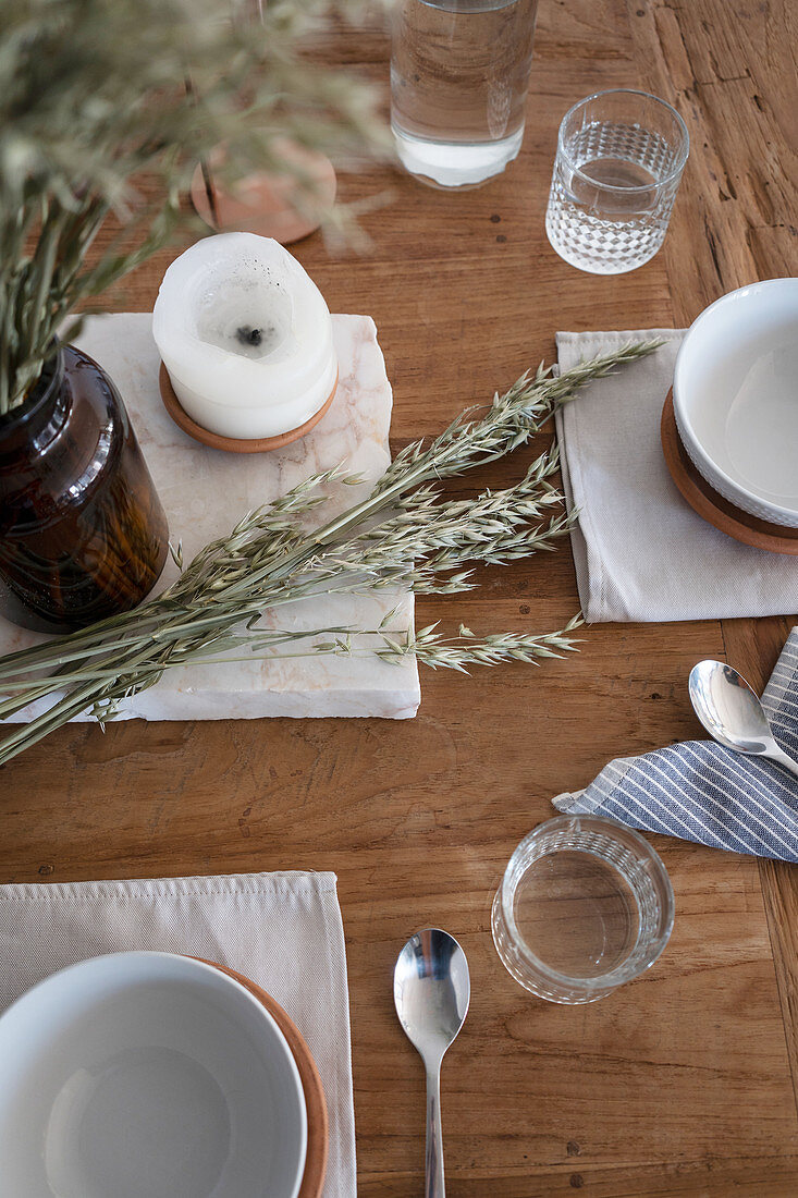 Place setting, candle and ears of cereal on rustic wooden table