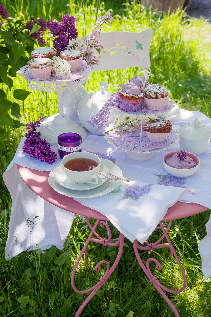 Gedeckter Tisch mit Muffins, Tee und Fliedern im Garten
