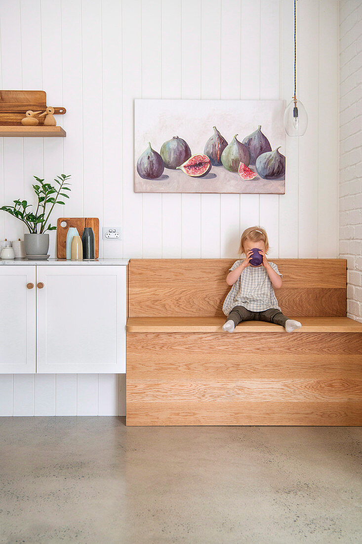 Kleines Mädchen sitzt trinkend auf einer Holzbank in der Küche