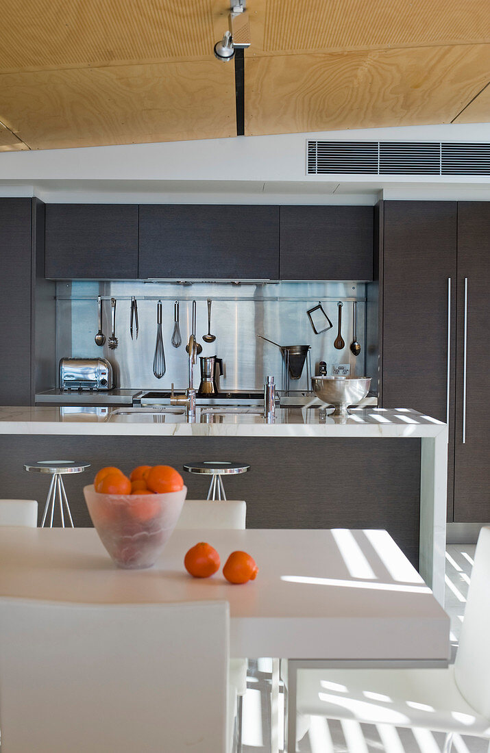 Weißer Esstisch mit Orangen, im Hintergrund anthrazitfarbene Einbauküche mit Kücheninsel