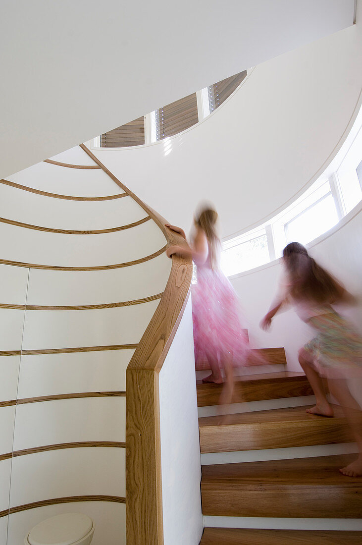 Two girls running up spiral staircase with wooden treads in white stairwell
