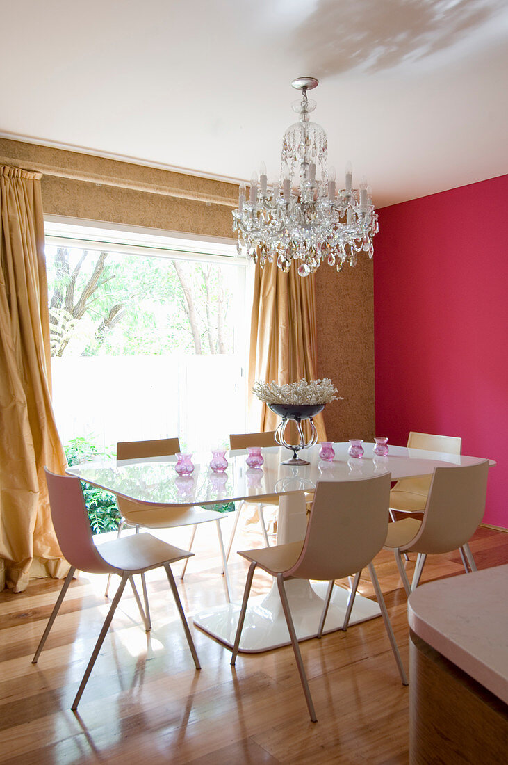 Designer-Esstisch mit Stühlen, darüber Kronleuchter im Esszimmer mit pinkfarbener Wand