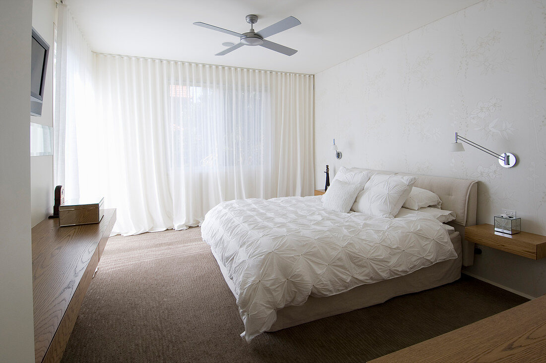 Doppelbett mit weißer Bettdecke und Kissen, Wandleuchte über schwebender Nachttisch im Schlafzimmer