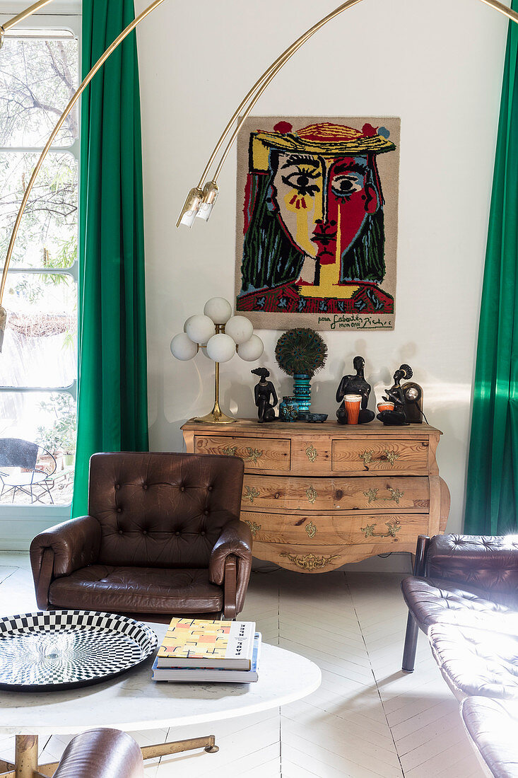 Gemälde über Holzkommode, im Vordergrund Couchtisch und Ledersessel im Wohnzimmer