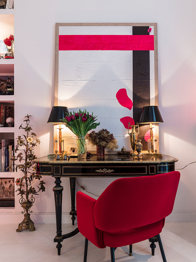 Red upholstered chair at antique table with table lamps and modern artwork