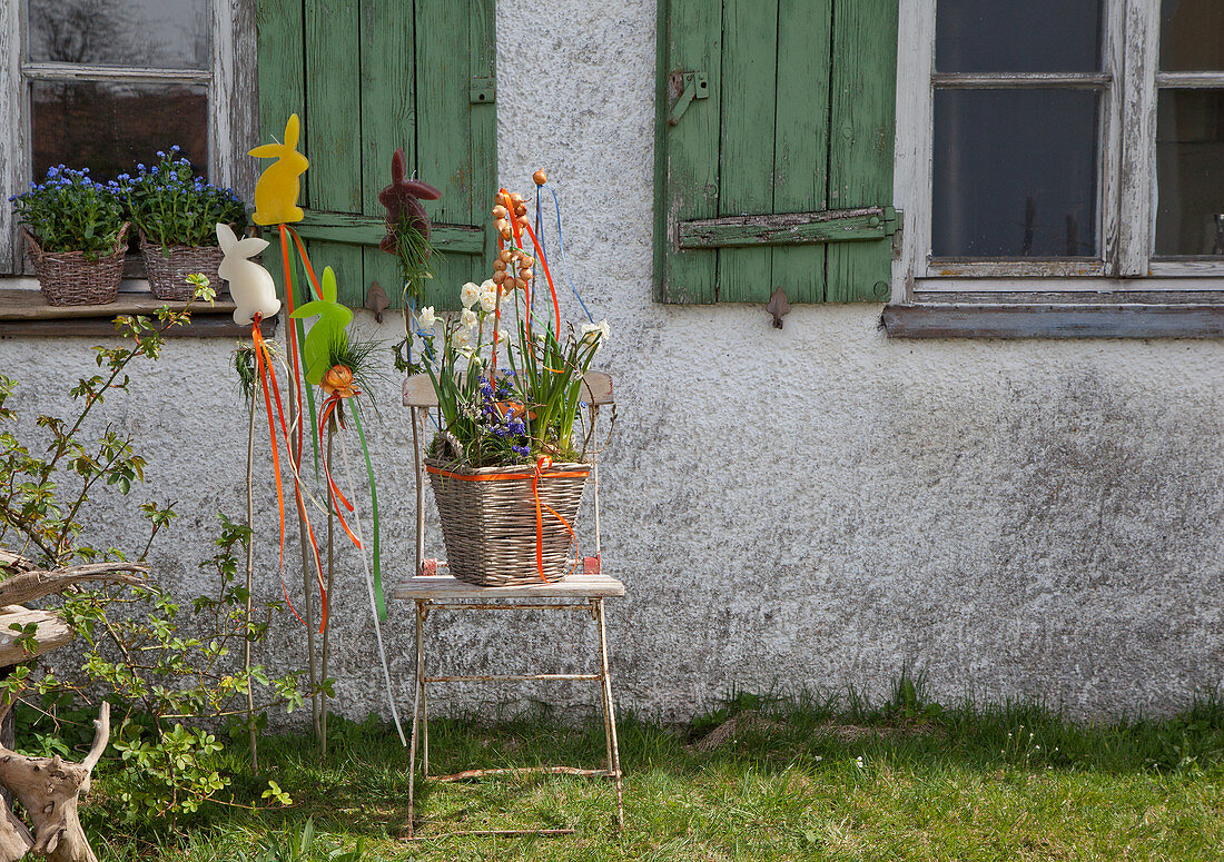 Easter arrangement in basket and Easter-themed garden stakes outside house