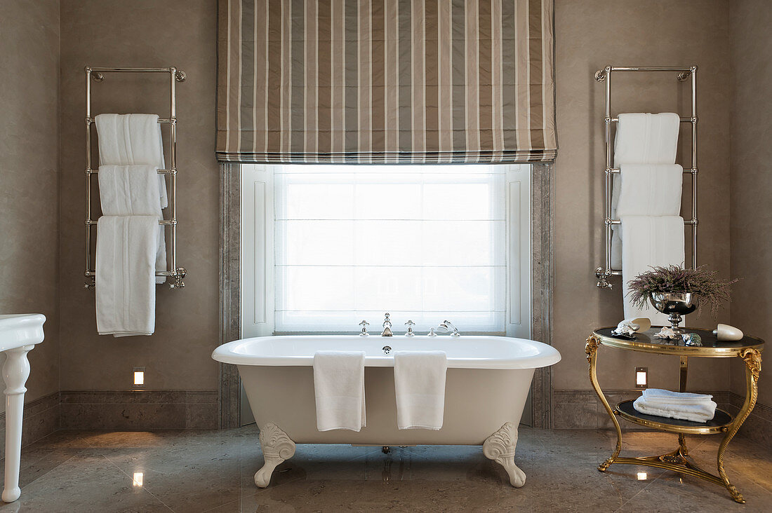 Frei stehende Badewanne mit Klauenfüssen vor Fenster im Badezimmer mit grauem Marmorboden
