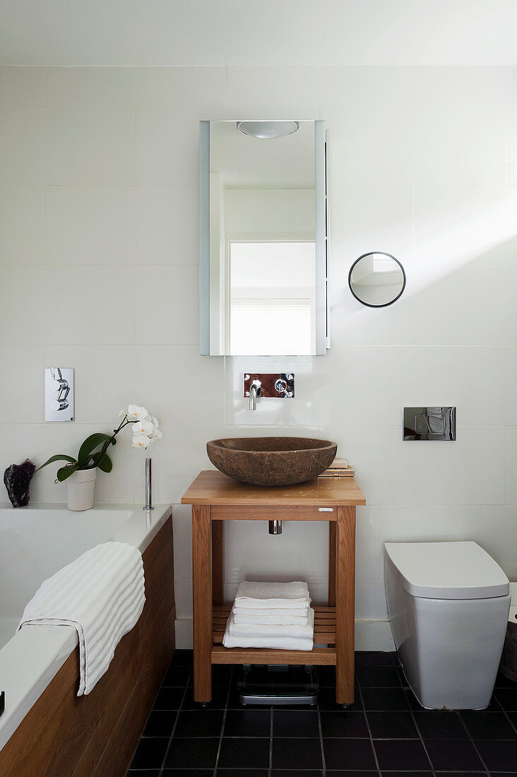 Stein-Waschschüssel auf Holzstisch zwischen Badewanne und Toilette im Badezimmer mit Schiefer-Fliesenboden