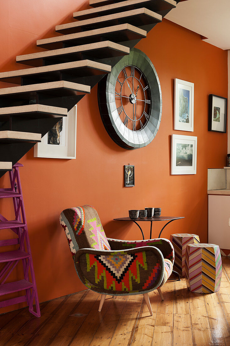 Kelimsessel vor orangefarbener Wand unter freitragender Treppe